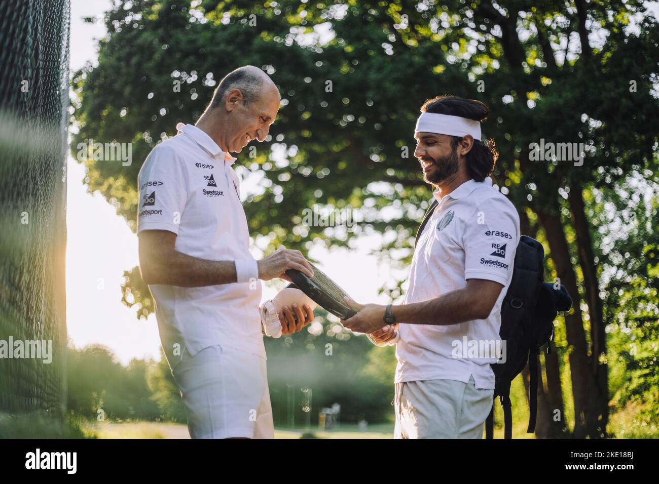 Seitenansicht lächelnder männlicher Freunde, die beim Halten des Tennisschlägers reden Stockfoto