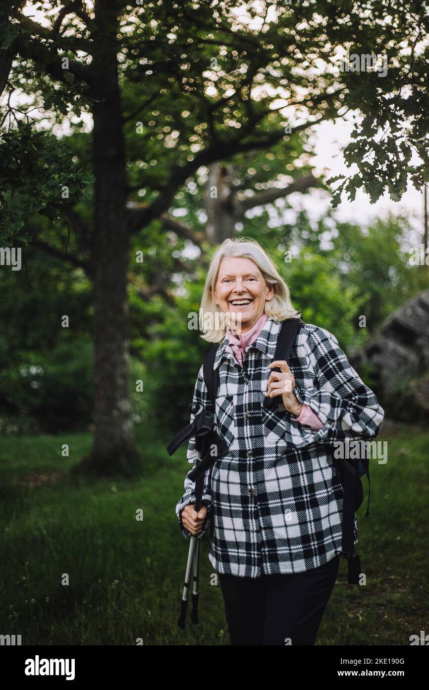 Porträt einer glücklichen älteren Frau, die beim Wandern im Wald Wanderstöcke in der Hand hält Stockfoto