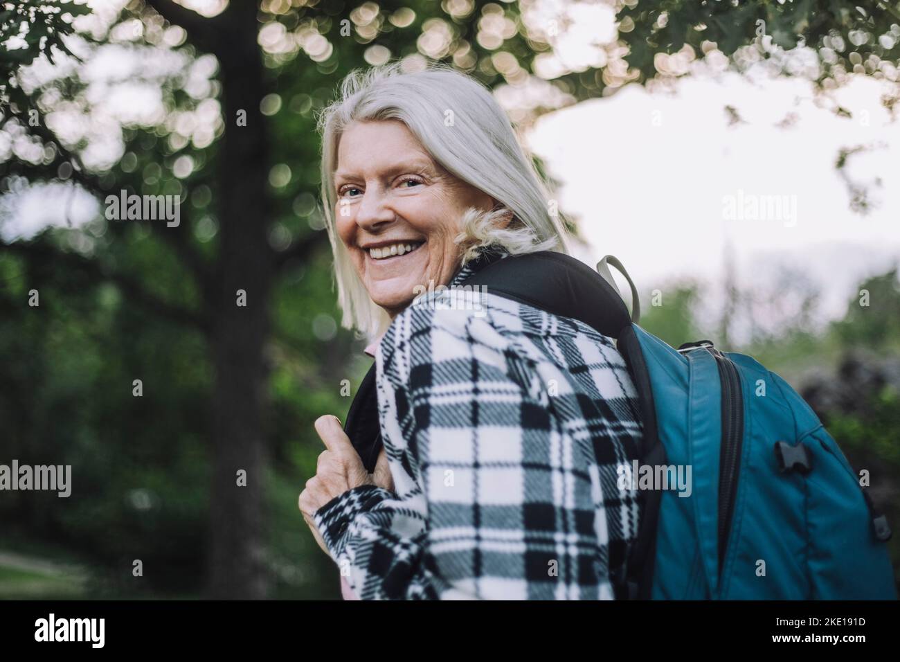 Porträt einer glücklichen älteren Frau, die beim Wandern über die Schulter blickt und dabei den Rucksack trägt Stockfoto