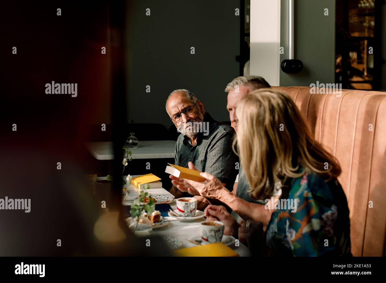 Älterer Mann, der Freunde und Freundinnen anschaut, die über das Buch im Café diskutieren Stockfoto