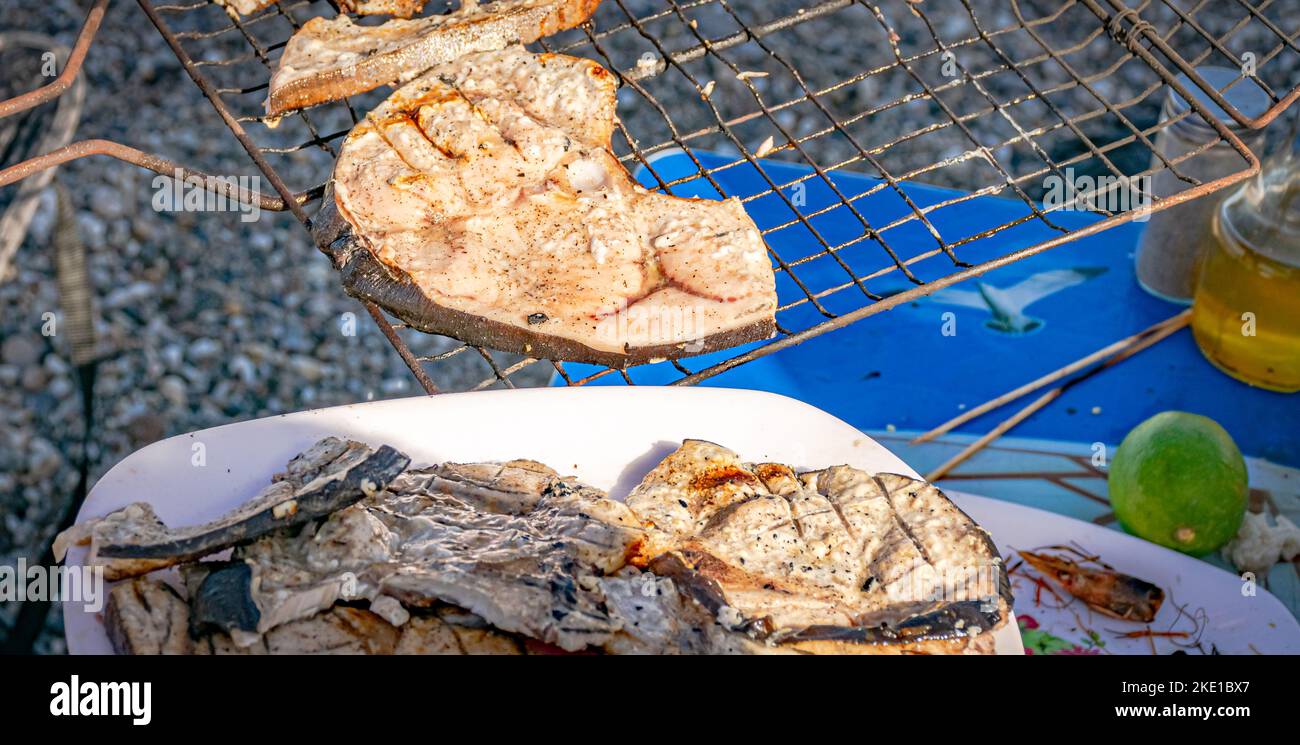 Schwertfischscheiben auf einem weißen Teller und auf einem grill. Selektiver Fokus auf Vordergrund und verwischten Hintergrund mit einer Zitronenfrucht und einem Krabbenkopf Stockfoto