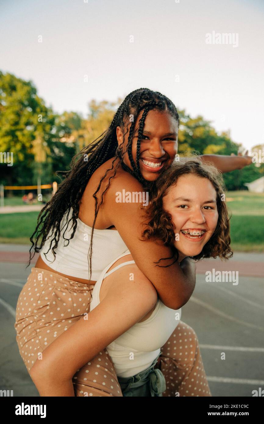 Portrait von glücklichen Teenager-Mädchen geben Huckepack Fahrt zu einem fröhlichen Freund im Park Stockfoto