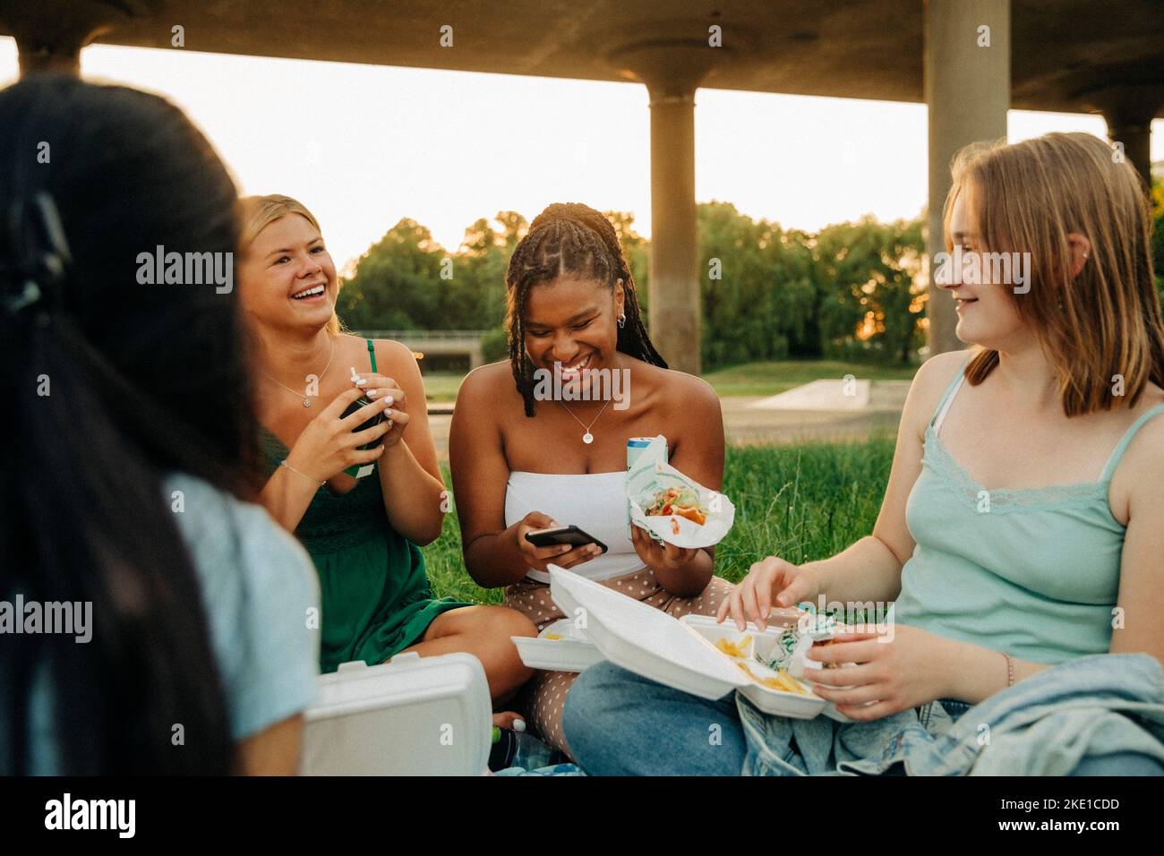 Glückliche Teenager-Mädchen, die sich unterhalten, während sie das Essen im Park genießen Stockfoto