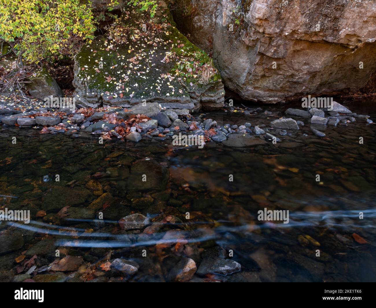 Küstenfelsen, herbstliches Laub, Bachfelsen und andere Details stehen im Kontrast zu streifenden Schaumstoffpunkten, die durch ein Riffel direkt stromaufwärts und durch die Strömung entstehen Stockfoto