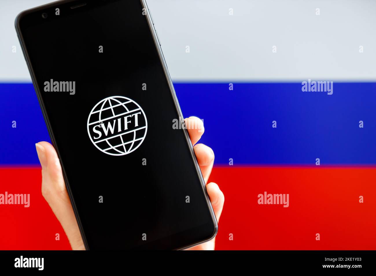 Ukraine, Kiew - Februar, 23 2022: Handhaltemobil mit SWIFT-Logo und russischer Flagge im Hintergrund. Sanktionen gegen Russland, Trennung von SW Stockfoto