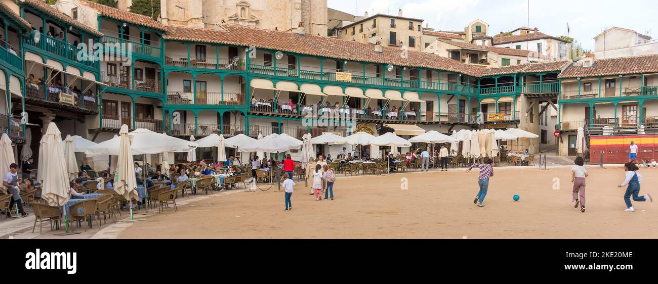 Die Gäste sitzen an Tischen auf Balkonen und am Boden um den zentralen platz (der auch als Stierkampfarena fungiert), während die Kinder in der spanischen Stadt Fußball spielen Stockfoto