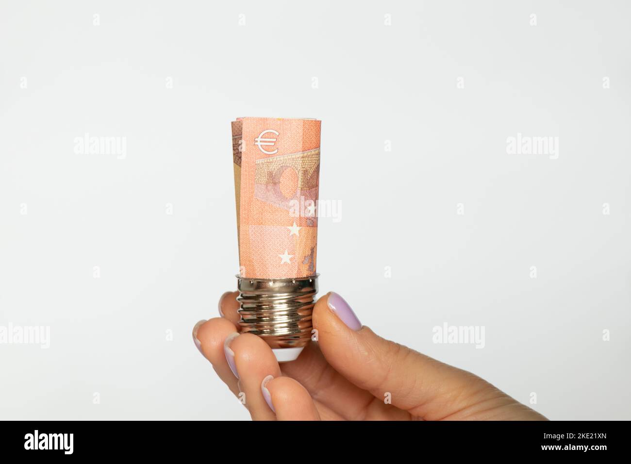 Eine Frauenhand hält eine Patrone aus einer Glühbirne mit Euro auf weißem Hintergrund, der Preis für Strom, Technologie Stockfoto