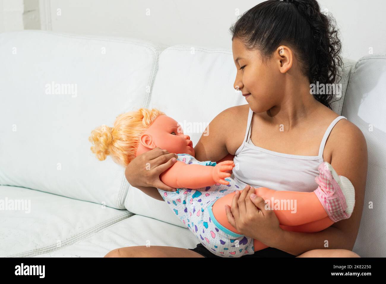latina Brünette Mädchen, spielt mit der Puppe, als wäre es ihre Tochter. Das kleine Mädchen hält ihre Puppe, als wäre es real. Stockfoto