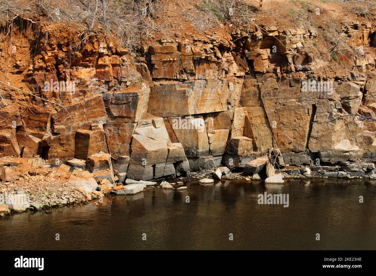 Rot-gelbe Felsklippe über dem Fluss. Das Konzept des Bergbaus. Stockfoto