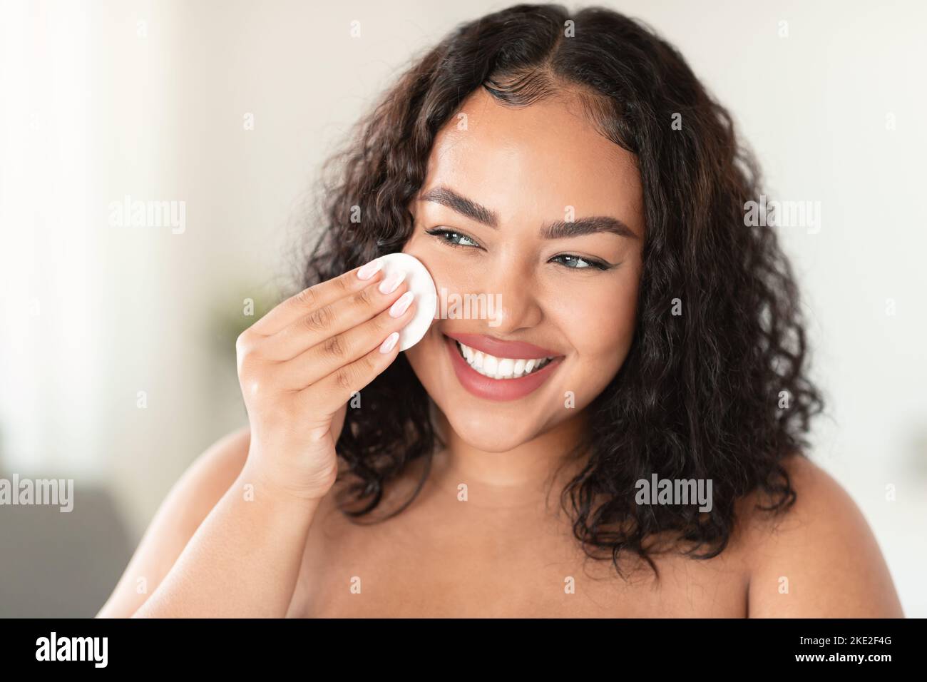 Nahaufnahme Porträt einer glücklichen schwarzen übergroßen Frau mit Wattebausch, Löschen Make-up aus ihrem Gesicht, Anwendung Reinigungsmilch Stockfoto