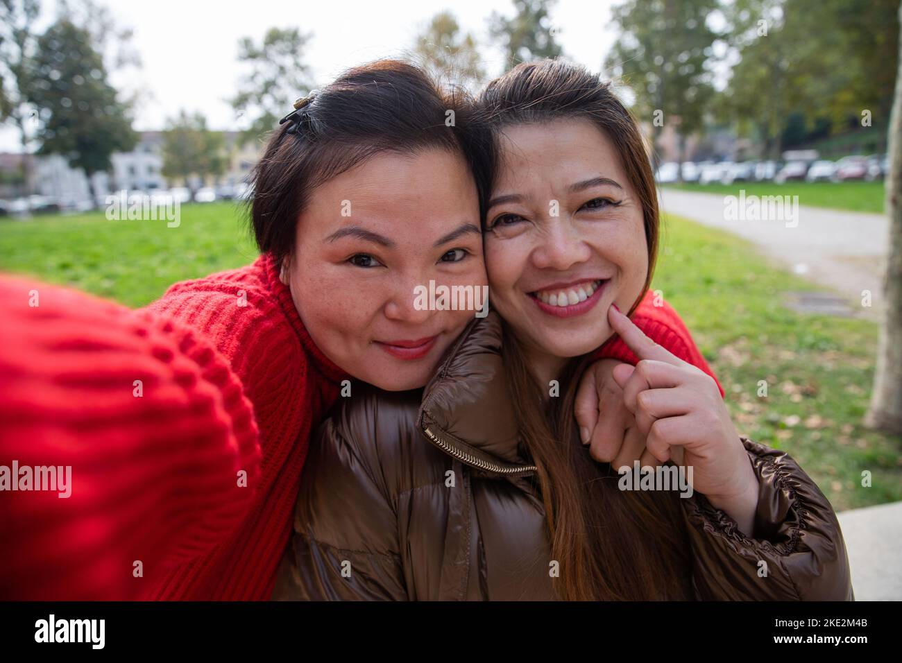 Zwei wunderschöne lächelnde chinesische Freundinnen machen ein Selfie in einem öffentlichen Park. Stockfoto