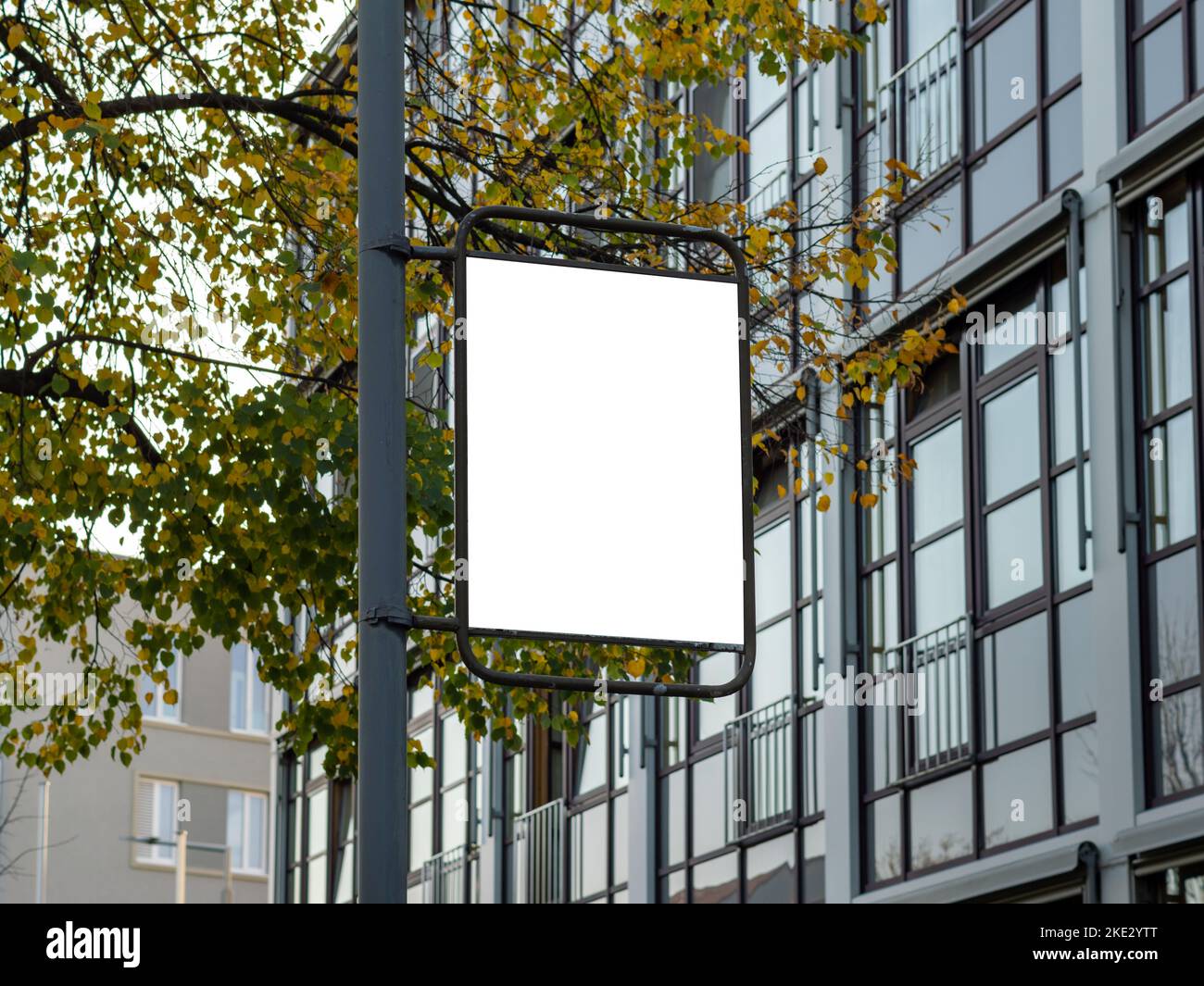 Vorlage für eine Werbung auf einem Lichtpfosten. Leerer weißer Bereich zum Testen eines Posterdesigns. Marketing in einem öffentlichen Bereich mit einem Bürogebäude. Stockfoto