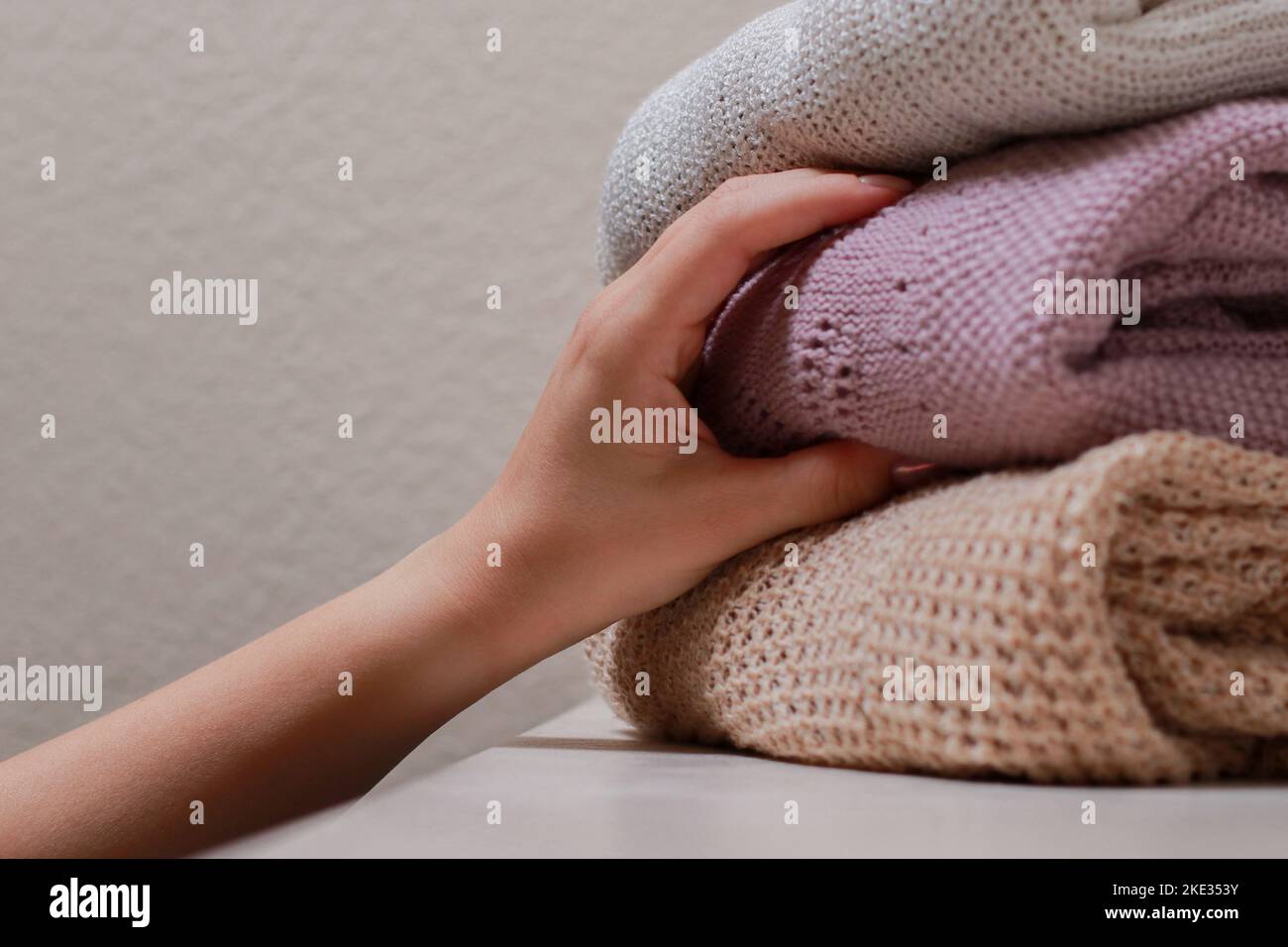 Nahaufnahme einer weiblichen Hand, die einen Pullover mit einem Stapel gefalteter Strickwaren ergreift Stockfoto