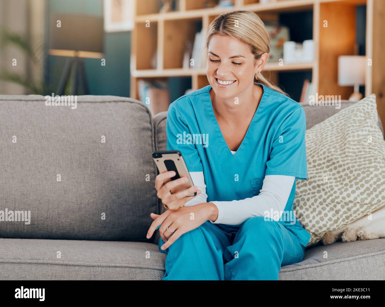 Krankenschwester, Telefon und glücklich mit Social Media, Post oder lustige Meme auf dem Sofa in zu Hause. Frau mit Gesundheits-, Medizin-und Wellness-App auf mobile Technologie oder Stockfoto