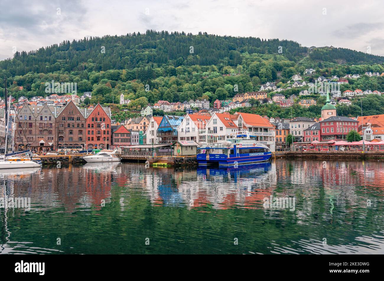 Bergen, Norwegen - 15 2022. August: Blick auf die Uferpromenade und die Kais (Bryggen) mit dem Berg Fløyen (einer der sieben Berge, die die Stadt umgeben) in Th Stockfoto