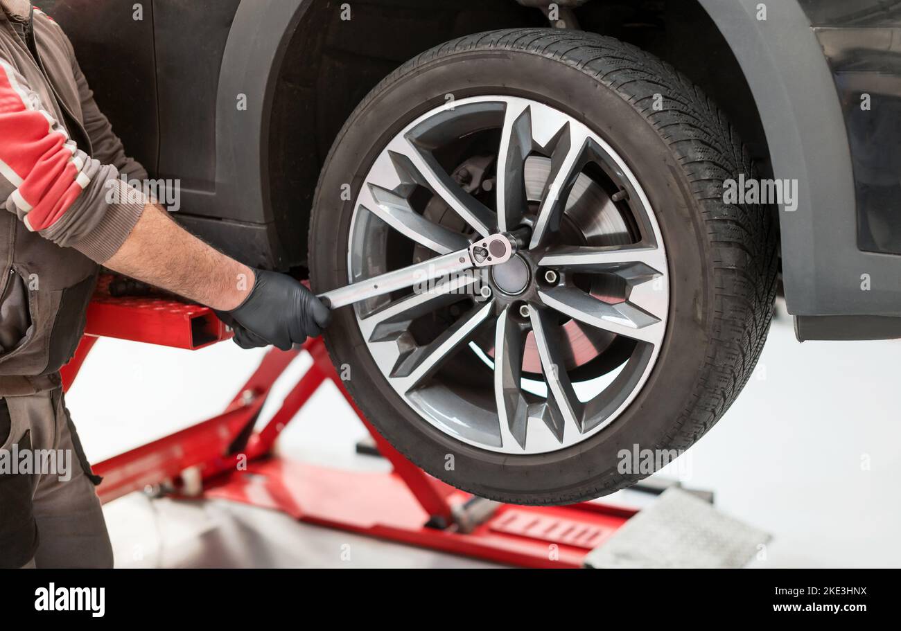Crop man in Uniform mit Drehmomentschlüssel Reifen aus dem Auto auf Hydraulikheber während der Arbeit in der Garage zu entfernen Stockfoto