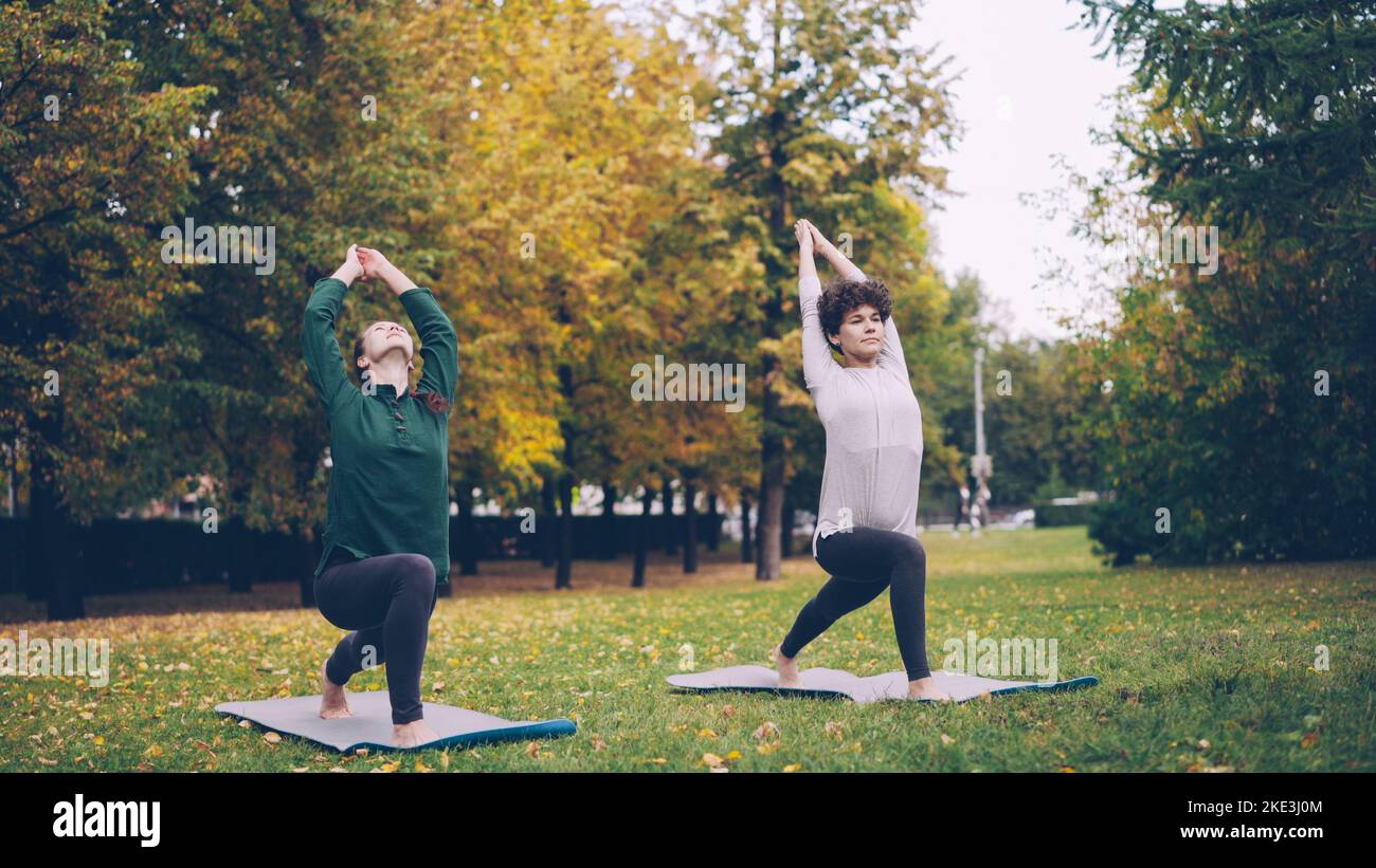 Slender Girl Yoga Student lernt Eagle Pose unter Anleitung eines erfahrenen Lehrers während der individuellen Praxis mit Lehrer im Park. Schöne Herbstnatur ist im Hintergrund. Stockfoto