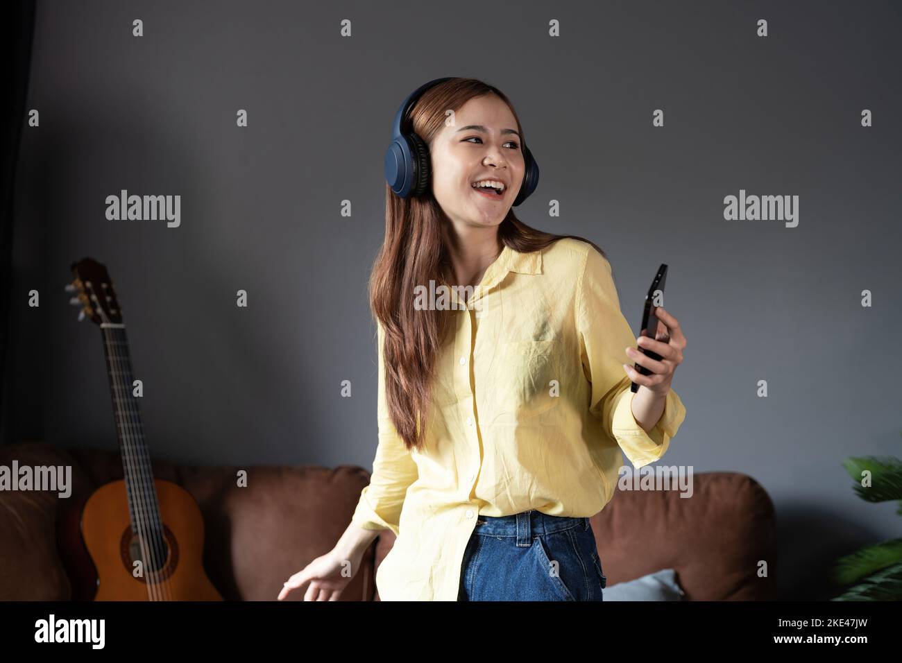 Fröhliche Frau, die Musik über kabellose Kopfhörer hört, die zu Hause auf dem Sofa stehen. Stockfoto