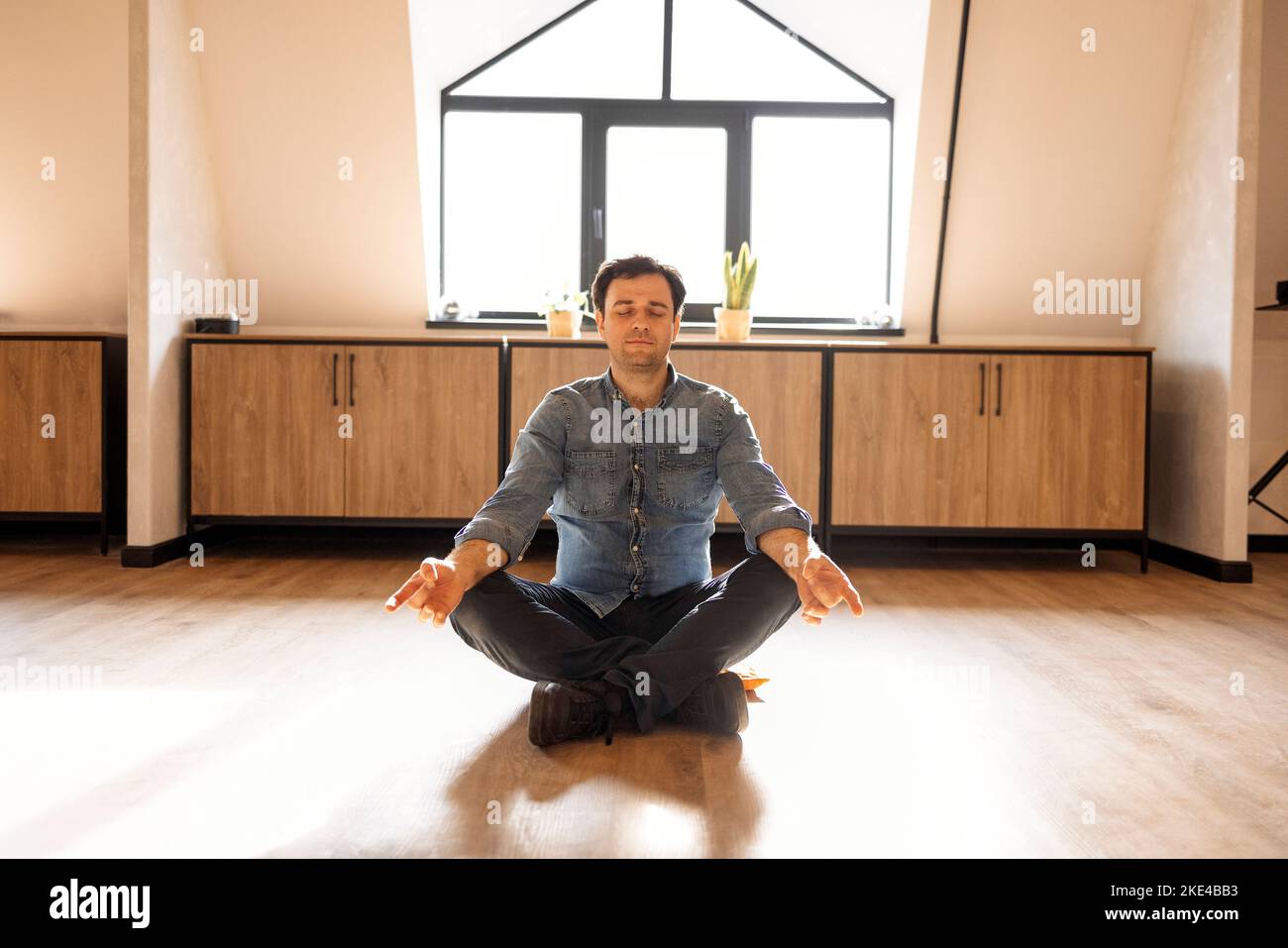 Gutaussehender hispanischer Mann trägt Jeans Casual Shirt sitzt auf dem Boden zu Hause entspannen, Meditation Geste mit den Fingern zu tun. Yoga-Konzept Stockfoto
