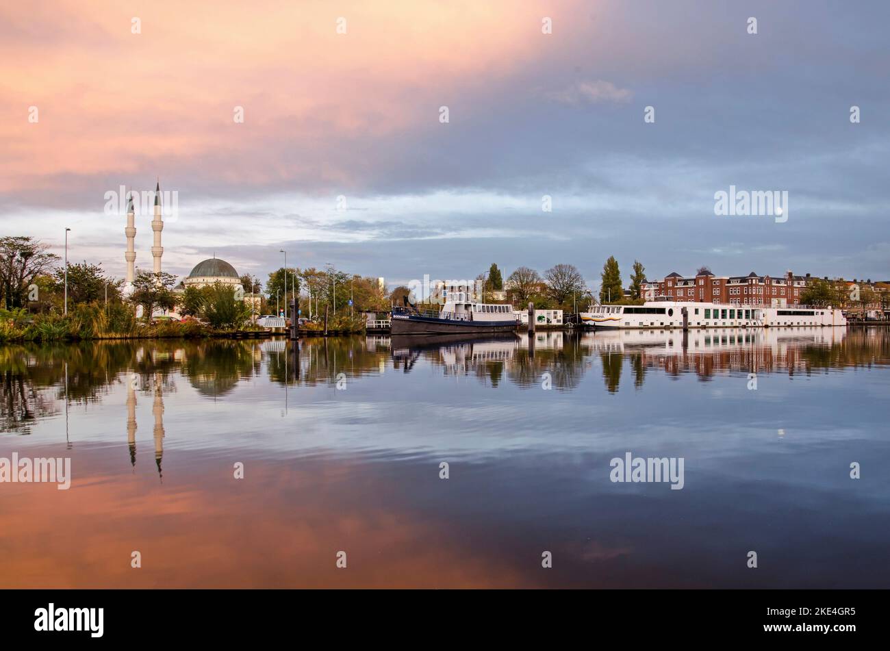 Rotterdam, Niederlande, 4. November 2022: Blick über das glatte Wasser des Delfshavense Schie Kanals in der Dämmerung, mit der Mevlana Moschee und einer Crui Stockfoto