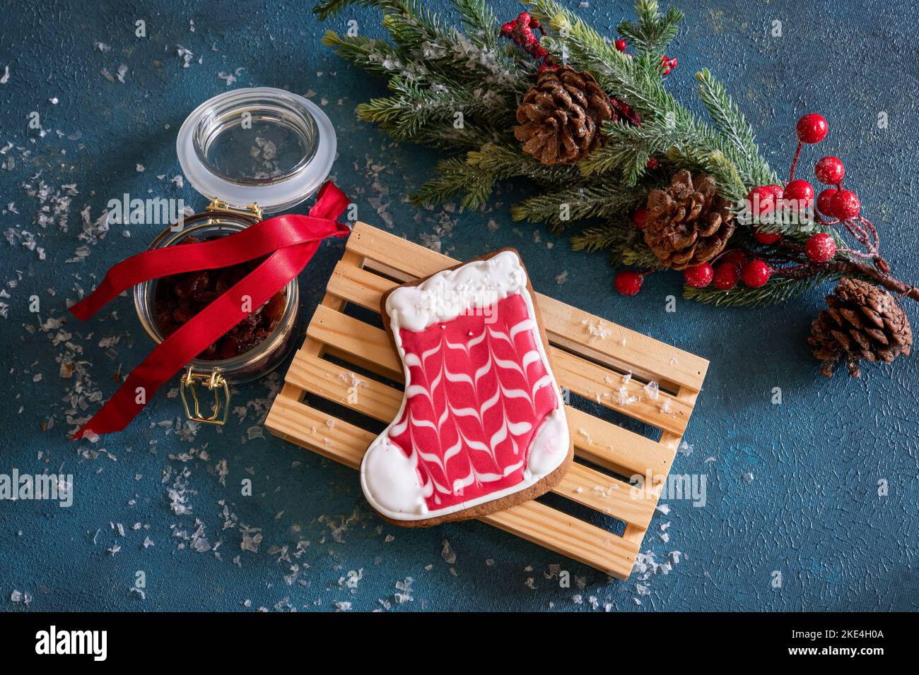 Weihnachts-Lebkuchen liegt auf einem Holzbrett. Auf dem Tisch liegt ein Fichtenzweig mit Zapfen und Beeren, daneben ein Glas Rosinen und Schnee. Stockfoto