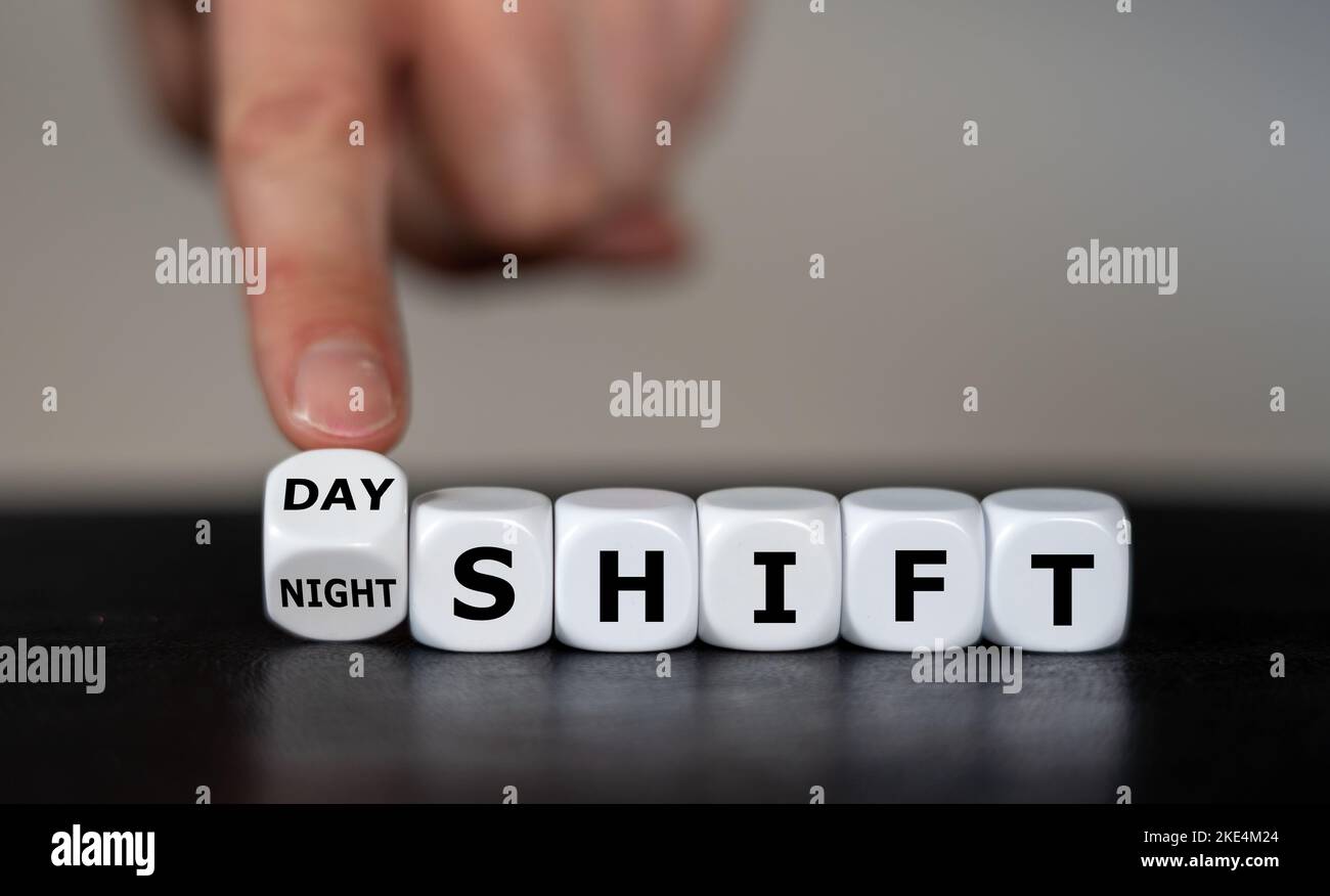Die Hand dreht Würfel und ändert den Ausdruck „day shift“ in „night shift“. Stockfoto