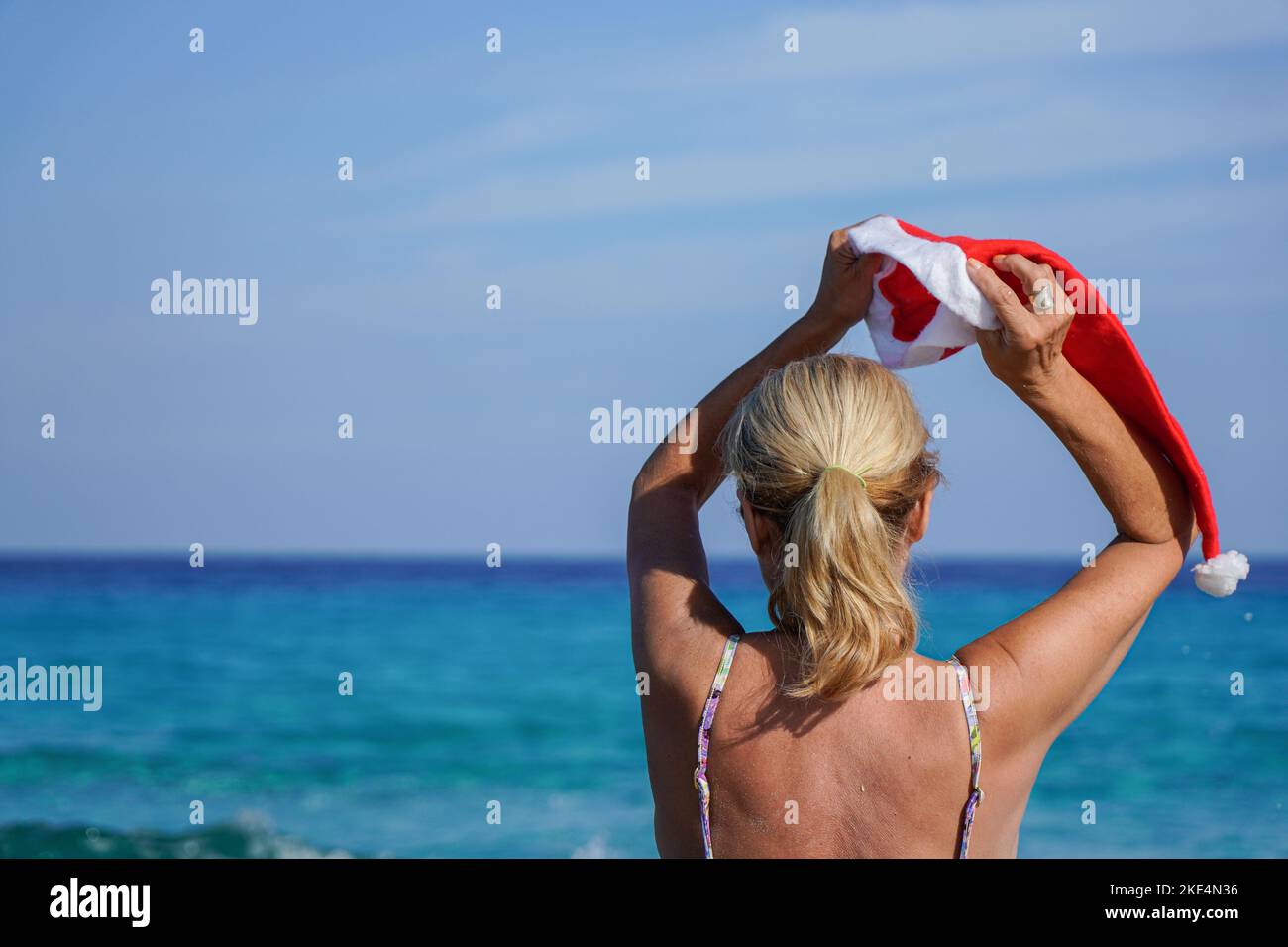 Frau, die einen weihnachtsmann-Hut an einen Strand setzt. Weihnachtsferien Stockfoto
