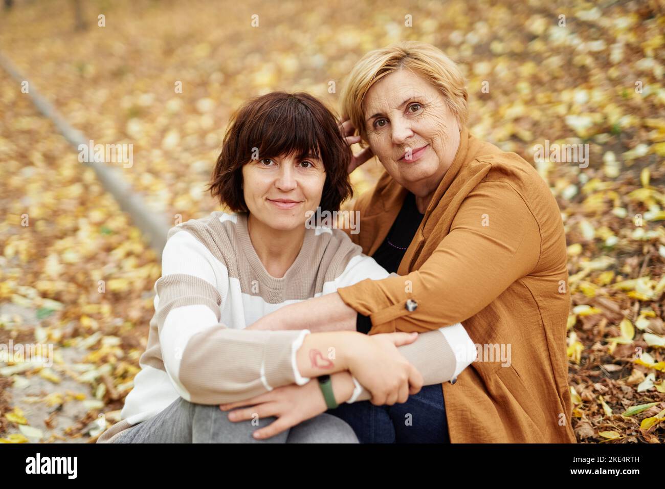 Ältere Rentnerin, Mutter und Erwachsene, fröhliche Tochter, verbringen in der Fallsaison gemeinsam Zeit im Freien im Park. Fröhliche kaukasische Mutter und ihre Tochter sitzen im Herbstpark. Hochwertige Fotos Stockfoto