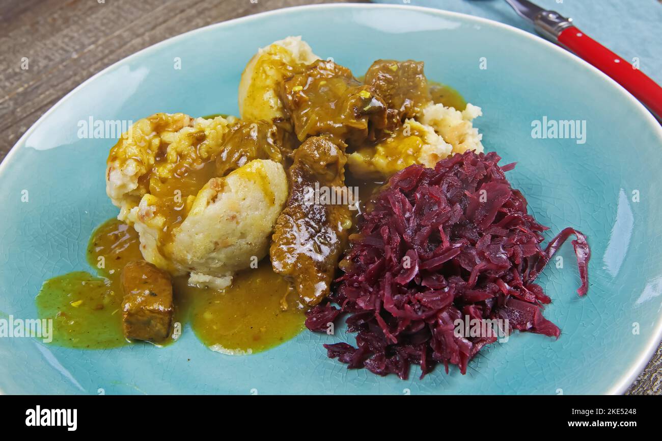 Typisch deutsche herzhafte hausgemachte rustikale Mahlzeit: Nahaufnahme von isolierten Knödeln, braune Soße, rot gekochter Kohl, Gulaschfleisch auf blauem Chi Stockfoto