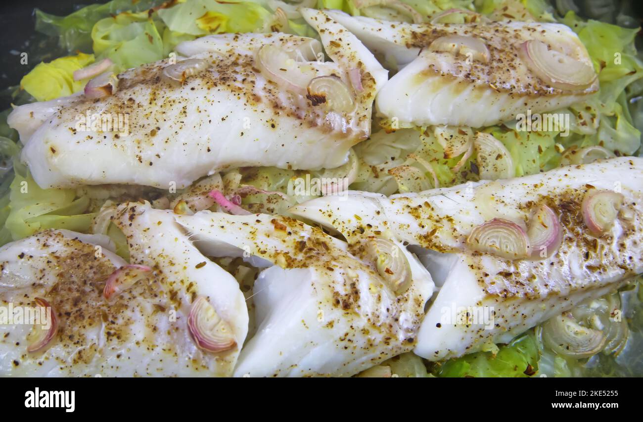 Zubereitung von Fischmehl: Isoliertes Ofenblech mit frisch gekochten hausgemachten gedünsteten Kabeljaufilets, pochiert auf Spitzkohl, gewürzt mit Zwiebeln, Kreuzkümmel Stockfoto