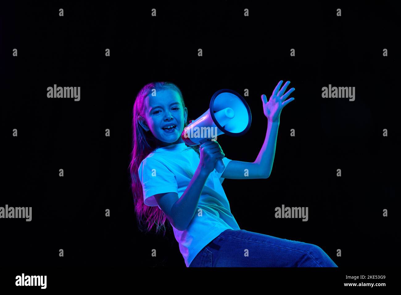 Porträt eines kleinen schönen Mädchen, Kind in weißem T-Shirt posiert, Gespräch auf Megaphon isoliert über schwarzem Studio-Hintergrund in Neonlicht Stockfoto