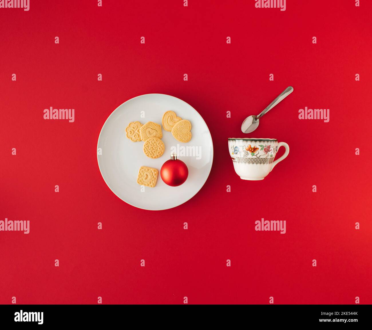 Minimale Komposition mit Weihnachtskeksen und roter Kugel auf weißem Teller und Teetasse mit Löffel. Konzept für das neue Jahr. Stockfoto