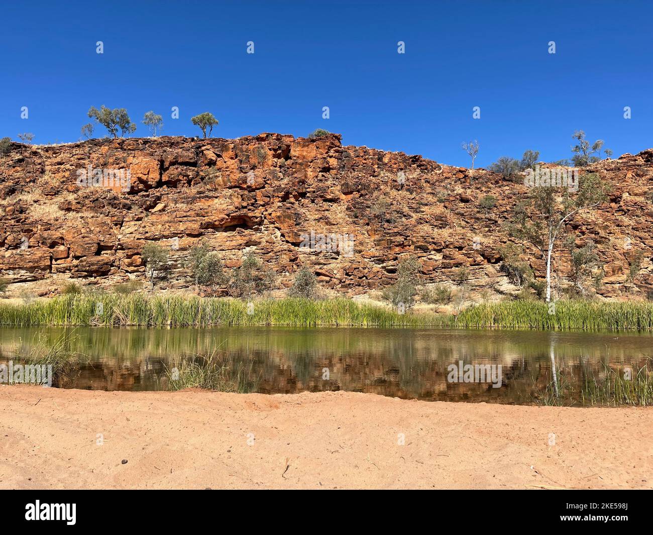 Eine malerische Aussicht auf den See, der an einem sonnigen Tag felsige Hügel und grüne Pflanzen an seinem Ufer reflektiert Stockfoto