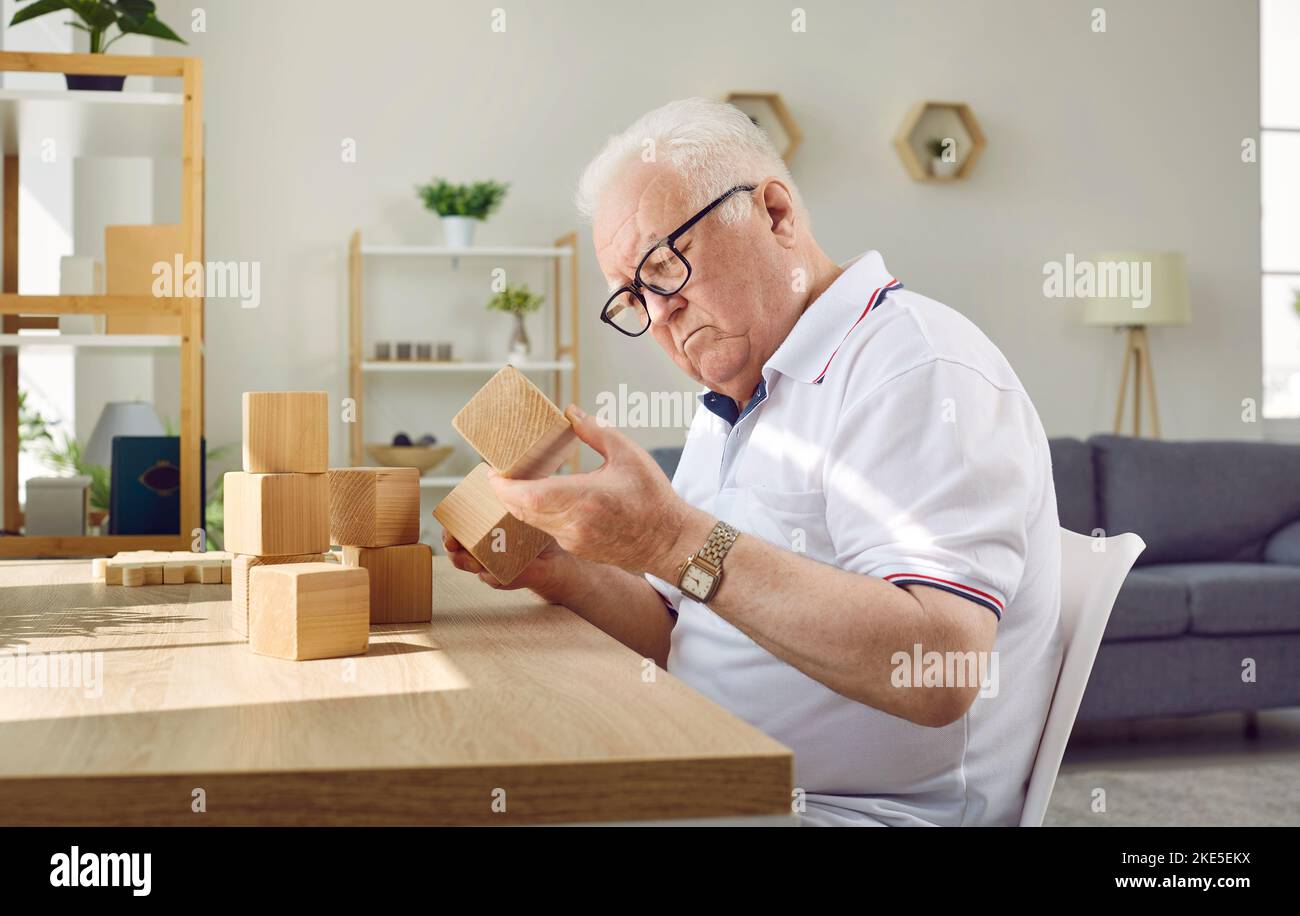 Demented Senior man mit Alzheimer-Krankheit sitzt am Tisch und spielt mit Holzwürfeln Stockfoto