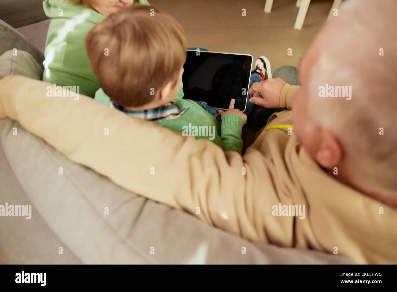 Rückansicht von Großvater und Enkel verbringen Zeit zusammen, mit Tablet zu Hause. Konzept von Emotionen, Familie, Glück, Fürsorge, Unterstützung und Freizeit Stockfoto