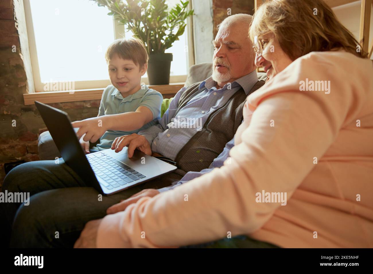 Lebensporträt einer freundlichen Familie, Großelterns und ihres Enkels, die auf dem Sofa sitzen und Zeit miteinander verbringen, mit modernen Gadgets, reden, studieren Stockfoto