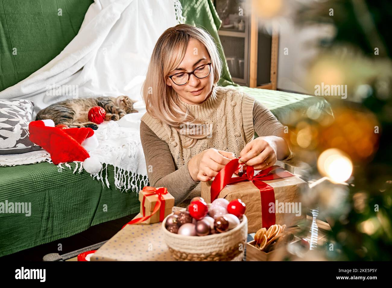 Geschenkverpackung von weihnachtsgeschenken. Blonde Frau Verpackung Geschenk in Recycling-Karte und dekorieren es mit rotem Band, getrocknete Orangen und Tannenzweige in der Nähe der Chris Stockfoto