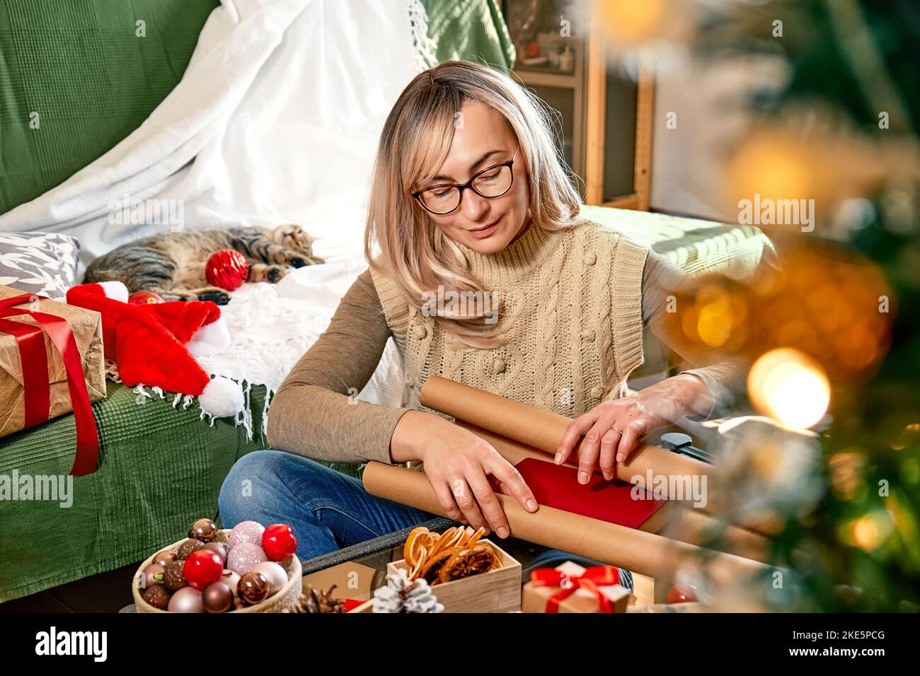 Geschenkverpackung von weihnachtsgeschenken. Blonde Frau wickelte ein Buch als Geschenk in recycelte Karte und dekorierte es mit getrockneten Orangen und Tannenzweigen in der Nähe der Christm Stockfoto