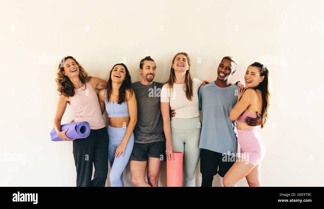 Eine Gruppe von glücklichen Fitness-Freunden lacht, während sie mit Yogamatten gegen eine Wand steht. Multikulturelle Menschen, die gemeinsam einen Yoga-Kurs besuchen. Sportliches Peo Stockfoto