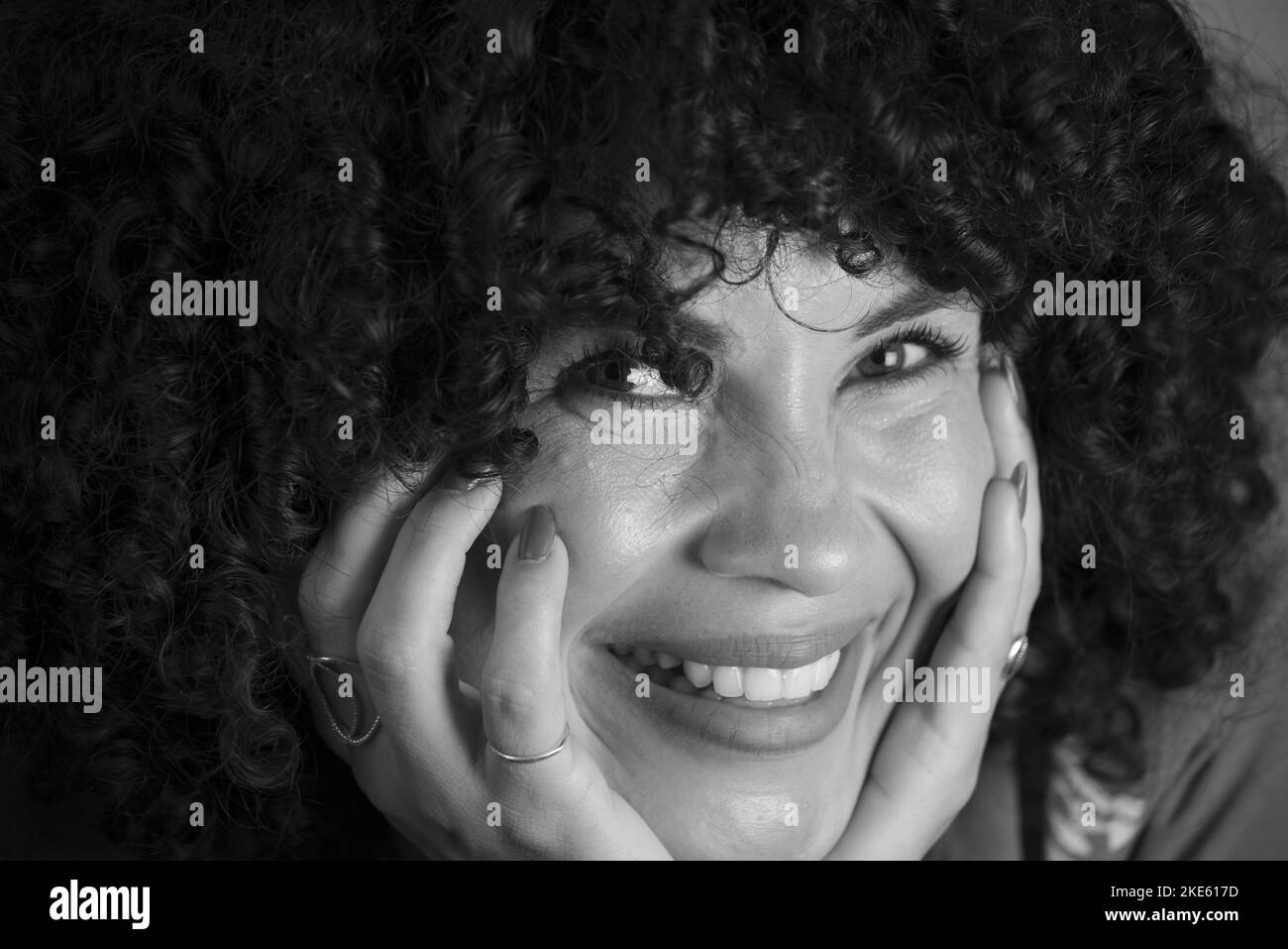 Schwarz-weißes Porträt einer Frau mit lockigem Haar. Schön und lächelnd vor hellem Hintergrund. Reife Frau. Selbstwertgefühl-Konzept. Stockfoto