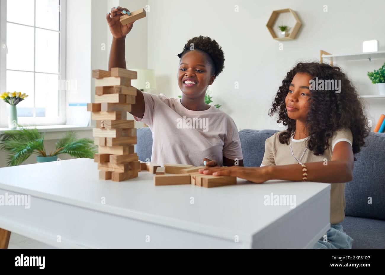 Lachende afroamerikanische Psychologin, die auf der Therapiestunde mit einem Teenager-Mädchen einen stürmenden Turm spielt. Stockfoto