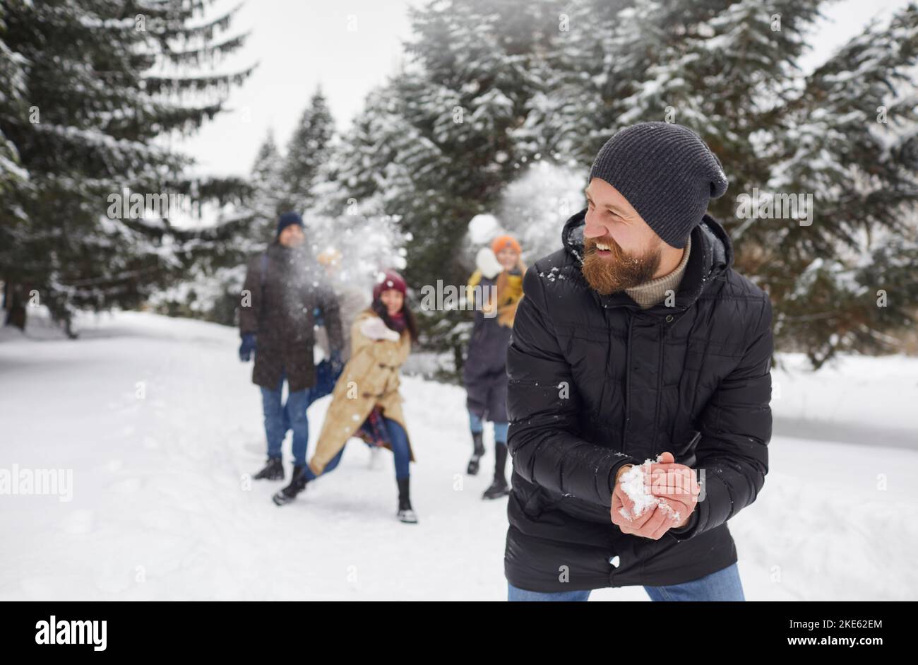 Lächelnde Freunde spielen Schneebälle und genießen den Winterurlaub im Freien Stockfoto