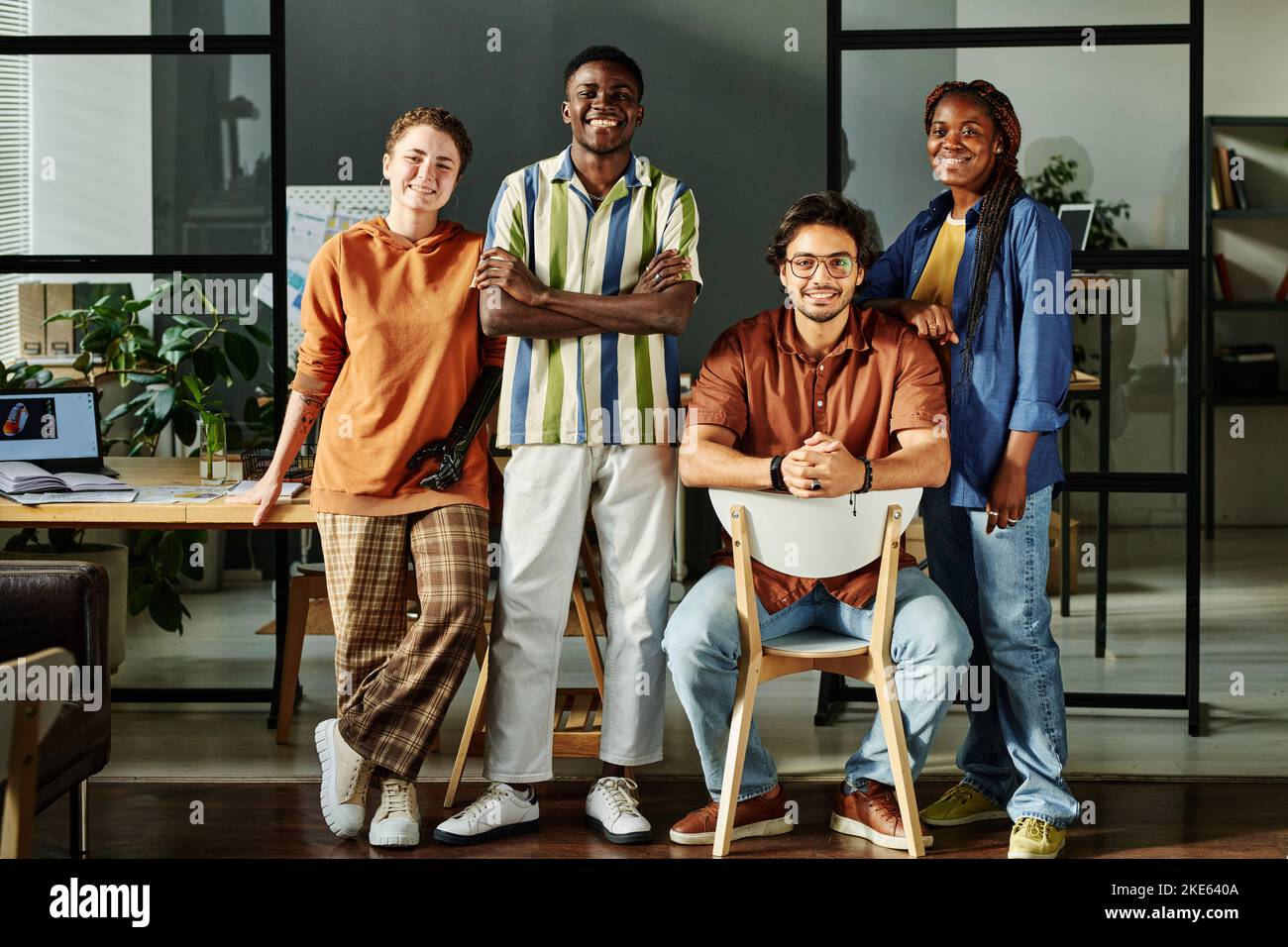 Eine Gruppe junger multikultureller Kollegen in Casualwear, die im Büro gegen den Arbeitsplatz stehen und lächelnd auf die Kamera blicken Stockfoto