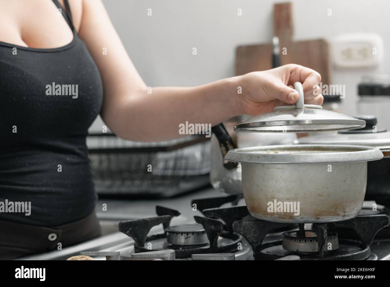 Junge Frau, die einen Topf auf dem Gasherd aufdeckte und den Deckel hob, um das Essen zu sehen, das sie vorbereitet. Stockfoto