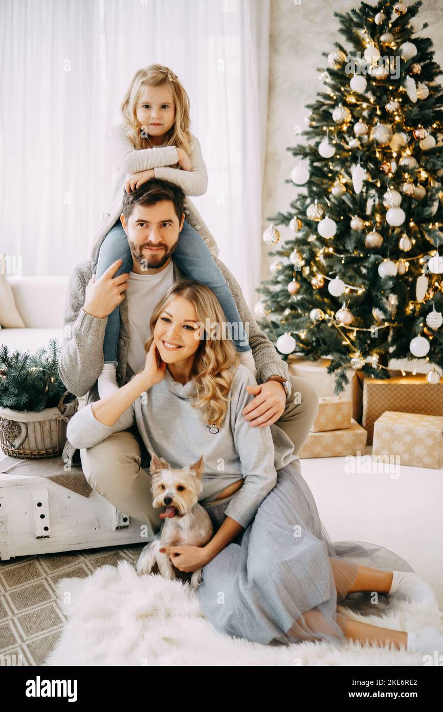 Glückliche Familie: Mama, Papa und Haustier. Familie in einem hellen Neujahrsraum mit einem Weihnachtsbaum. Stockfoto