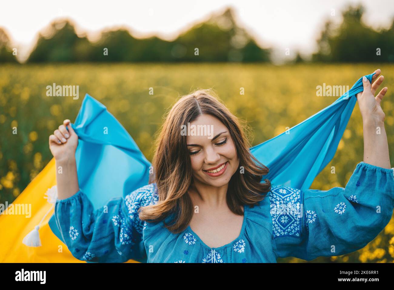 Glückliche ukrainische Frau mit Nationalflagge auf Rapsblüten Wiese Hintergrund. Stockfoto