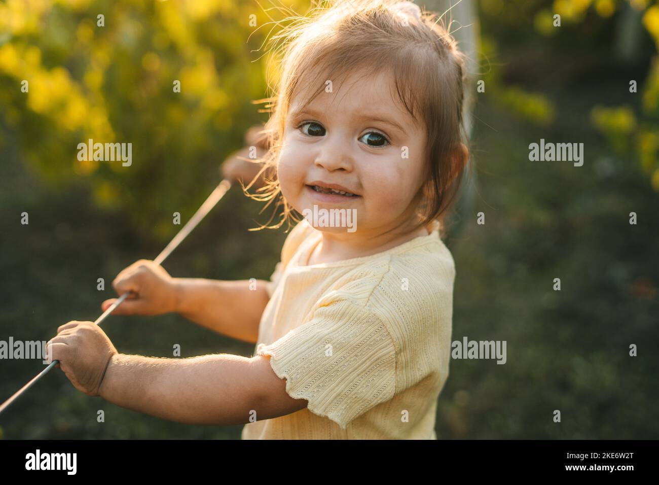 Porträt eines lächelnden kleinen Mädchens, das am Sommertag in den Reben des Gartens im Haus der Großmutter stand. Landleben, Ruhe und Sommer Stockfoto