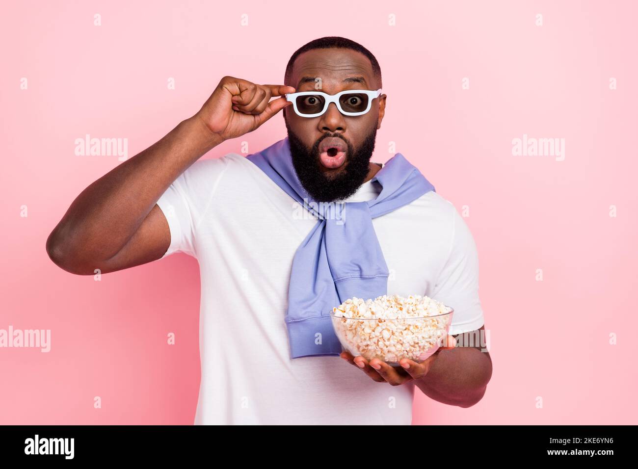 Foto von jungen beeindruckt Kerl sehen Horrorfilm in 3D Theater essen Snack isoliert auf rosa Hintergrund Stockfoto