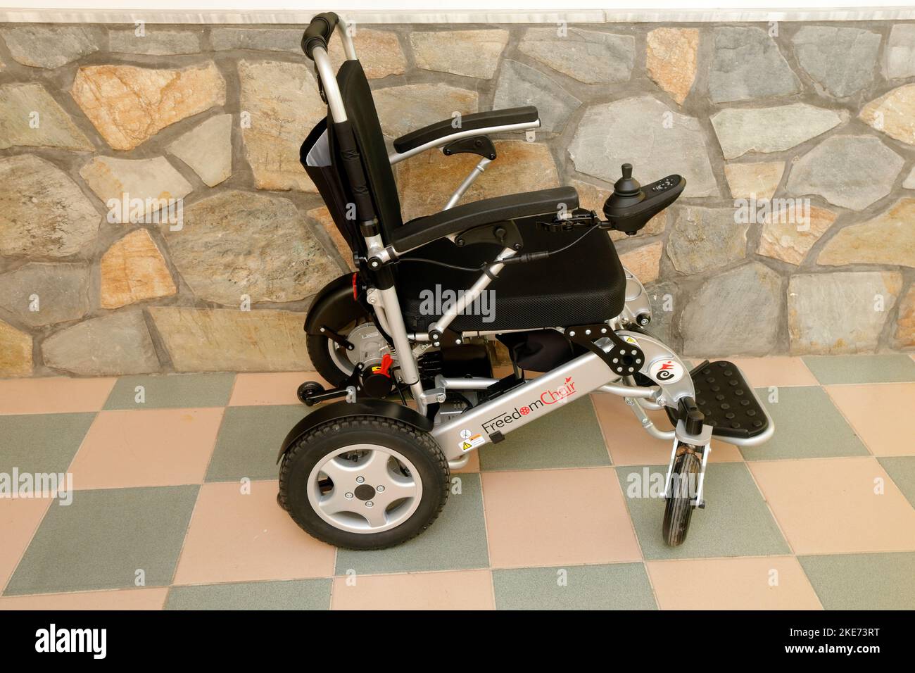 FreedomChair Rollstuhl auf eigene Faust vor einem Stein und Fliesen Hintergrund. Stockfoto