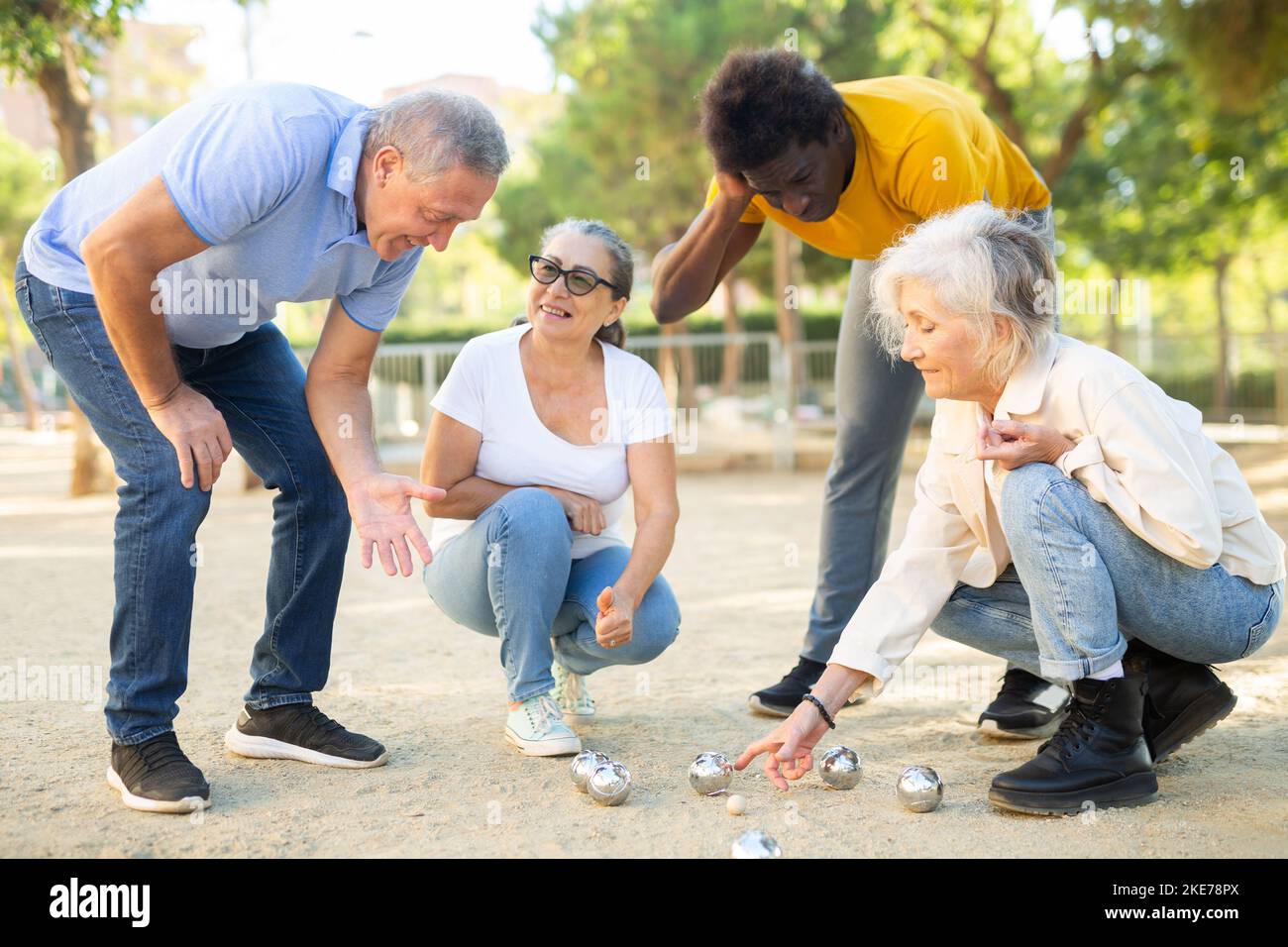 Multirassische reife Erwachsene Menschen messen Abstand zwischen den Kugeln in Petanque Spiel draußen in einem Park Stockfoto